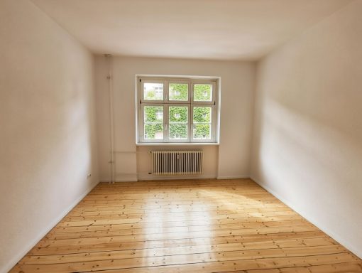 Fachgerechte Malerarbeiten im Wohnzimmer mit spritzlackiertem Radiator, lackiertem Fenster und abgezogenem Dielenboden